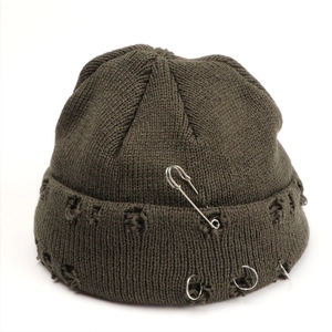Close-up of olive green distressed knit beanie with metal safety pin and ring details