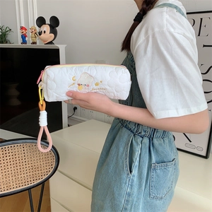Detail of white quilted pencil case featuring cartoon embroidery and colorful woven lanyard
