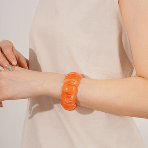 Detail of an orange acrylic cuff bracelet with marble texture worn with minimalist attire