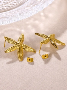 Detailed view of gold starfish stud earrings on textured fabric with earring backs