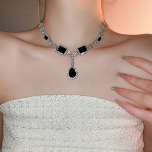 Detail of silver geometric necklace featuring black waterdrop stones on model neck