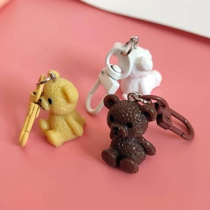 Three cute colorful resin mini bear pendants in yellow, white, and brown on pink background