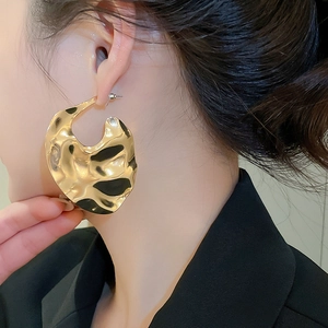 Close-up of large golden geometric earrings with hammered texture on a fashion model