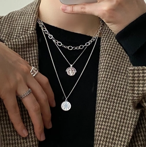 Detail of layered silver necklaces with coin pendants and engraved rings on model