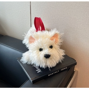 Detail of white plush Westie dog bag with red handles resting on a black book