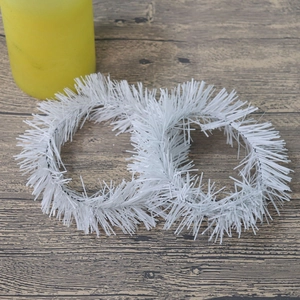 Close-up of two white tinsel Christmas wreaths on wooden surface with candle backdrop