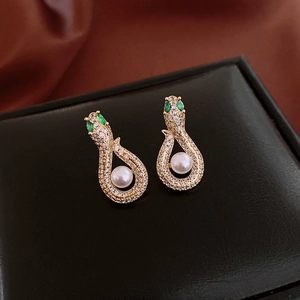 Macro shot of gold snake earrings with green stone eyes and pearl detail on black leather