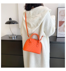 Detail of orange quilted shell bag with gold hardware and adjustable strap on a model