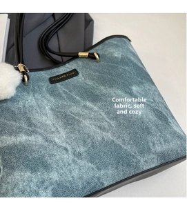 Detail of blue denim tote bag with black straps, golden hardware, and white fur charm
