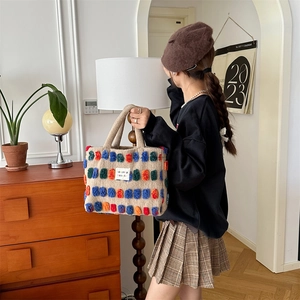 Detail of beige knit bucket bag featuring colorful 3D pom-pom accents and brand tag