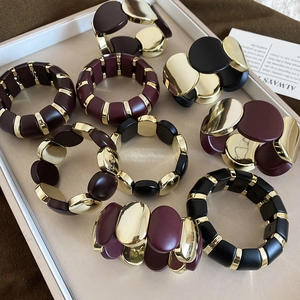 Detail view of oval acrylic stretch bracelets in burgundy and black with gold metal accents