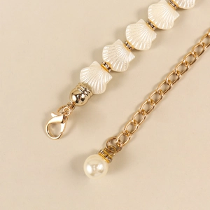 Detailed close-up of golden shell chain belt with sparkling rhinestones and pearl pendant