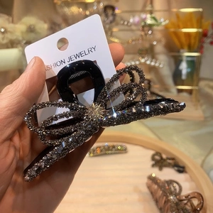 Detailed view of a large bow hair claw clip with dark rhinestones on a fashion display card