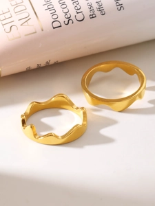 Detailed view of two 18K gold-plated wave rings with fluid melt design on a beige surface