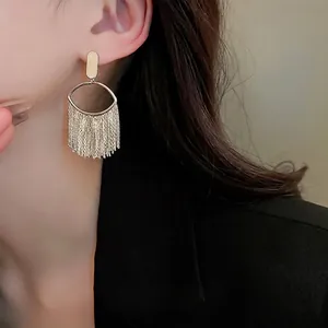 Golden oval tassel earrings with layered chain fringe worn by a model in a black suit