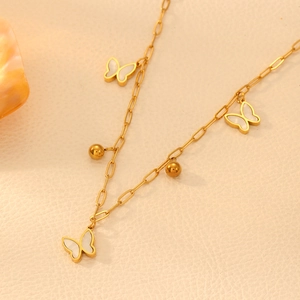 Detail of gold chain necklace featuring white butterfly charms and golden beads on beige fabric