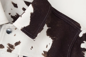 Close-up detail of cow print jacket featuring soft faux fur texture and silver metal button