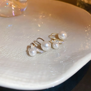 Macro shot of gold and silver pearl ear cuffs with zircons on a white ceramic plate