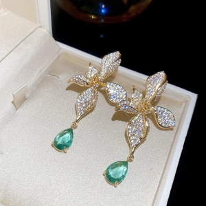 Macro shot of luxury flower drop earrings with champagne gold finish and green emerald zirconia