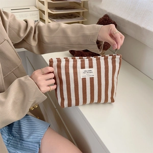 Brown and white striped fabric makeup bag held by a model in a bright interior setting