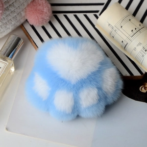 Detailed close-up of blue and white plush cat paw keychain with warm aesthetic background