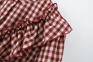 Detailaufnahme von burgunderfarbenem und beige kariertem Stoff mit Rüschen und Nähten