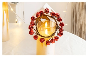 Macro detail of a red metal bell Christmas wreath around a warm glowing candle holder