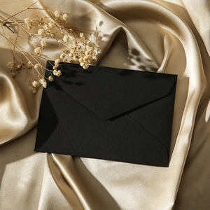Close-up of textured black paper envelope on champagne silk with dried flowers