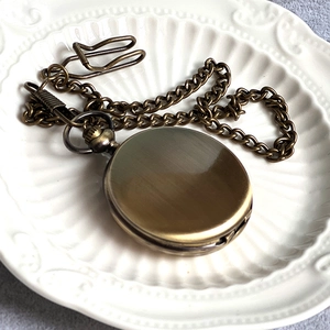Close-up of vintage bronze pocket watch with chain on decorative white ceramic plate