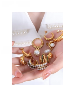 Detail of gold titanium steel earrings with pearls and green stones held by a hand