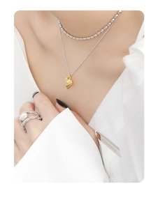 Macro detail of gold striped heart pendant layered with a silver bead necklace on a shirt