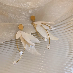 Nahaufnahme eleganter weißer Blütenohrringe mit goldener Fassung auf zartem Netzstoff
