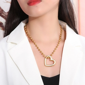 Close-up of a gold hollow heart pendant necklace with white crystals worn by a model