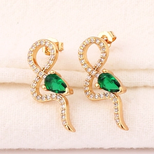 Macro shot of gold snake-shaped earrings with green pear-cut stones and white crystals