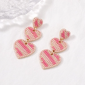 Pink seed bead woven triple heart drop earrings with rhinestones on a white fabric backdrop