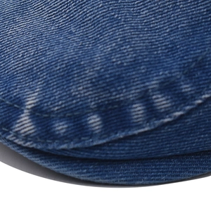 Détail des surpiqûres blanches et de la texture denim délavé sur une casquette bleue