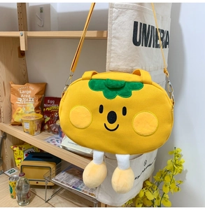 Detail of yellow persimmon-shaped canvas bag with green leaf decor and cartoon face