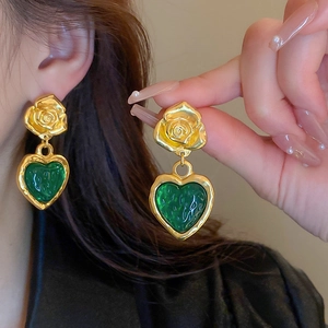 Close-up of a model wearing vintage green heart drop earrings with golden rose accents