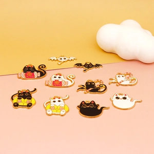 Detailed flat lay of Halloween cat and bat enamel charms with gold trim on pink backdrop