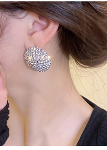 Close-up of sparkling oval stud earrings with pavé rhinestones worn by a model