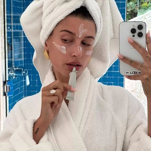 Detail shot of the light green lip balm tube held by a model in a bathroom mirror reflection