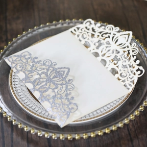 Detail of laser-cut glitter invitations with elegant floral patterns on glass tray