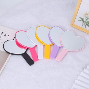 Detailed flat lay of heart-shaped handheld mirrors in six vibrant colors on white plush