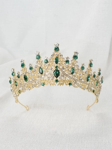 Detailed view of a golden tiara with emerald stones and rhinestones on white fabric