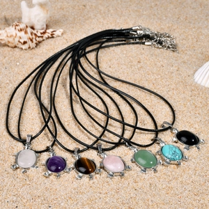Pendentifs tortue avec pierres naturelles colorées disposés sur un fond de sable