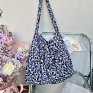Blue floral canvas tote bag with wide shoulder straps on a transparent chair