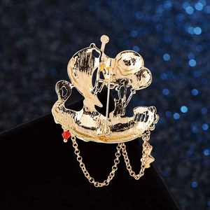 Golden sailboat brooch with metal chains and red bead pendant on blue background