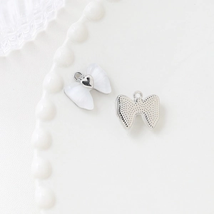 Macro shot of white enamel bow pendant with heart detail and textured silver metal back