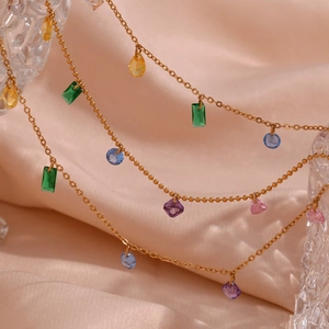 Macro shot of 18K gold necklace with colorful geometric zircons on pink silk background
