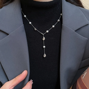 Detail of elegant Y-shaped pearl necklace featuring silver metal charms on a black sweater
